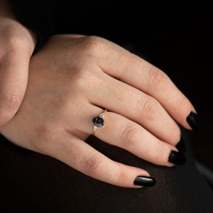 May include: A gold ring with a dark green oval gemstone and two smaller white gemstones on the band.
