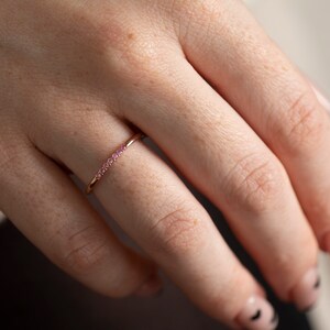 May include: A delicate rose gold ring with a row of small pink gemstones.