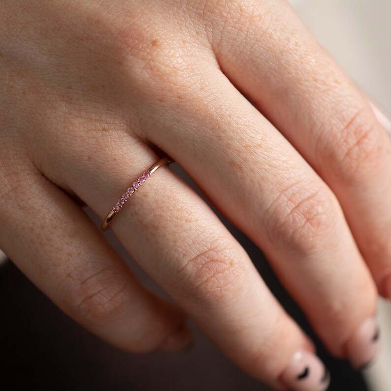 May include: A delicate rose gold ring with a row of small pink gemstones.