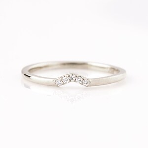 May include: A delicate silver band with a row of small diamonds set in a chevron shape.