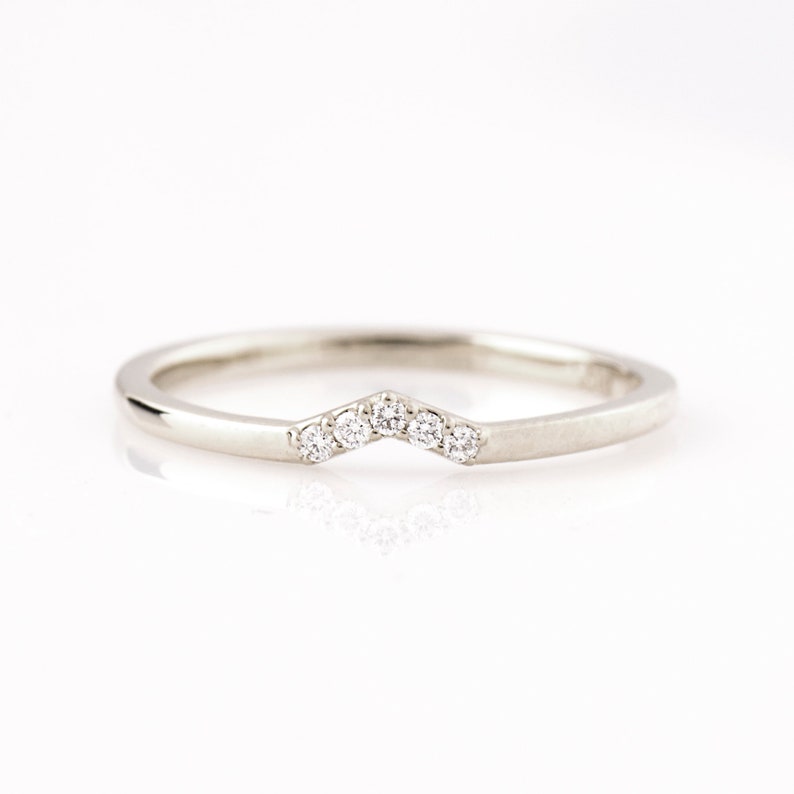 May include: A delicate silver band with a row of small diamonds set in a chevron shape.