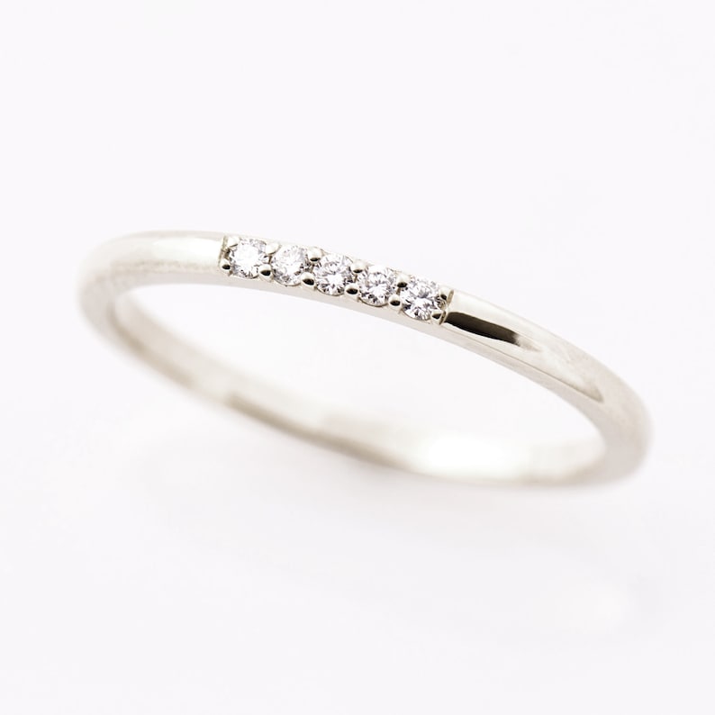 Op de afbeelding: Een dunne zilveren ring met een rij van vijf kleine diamanten die in het midden zijn gezet.