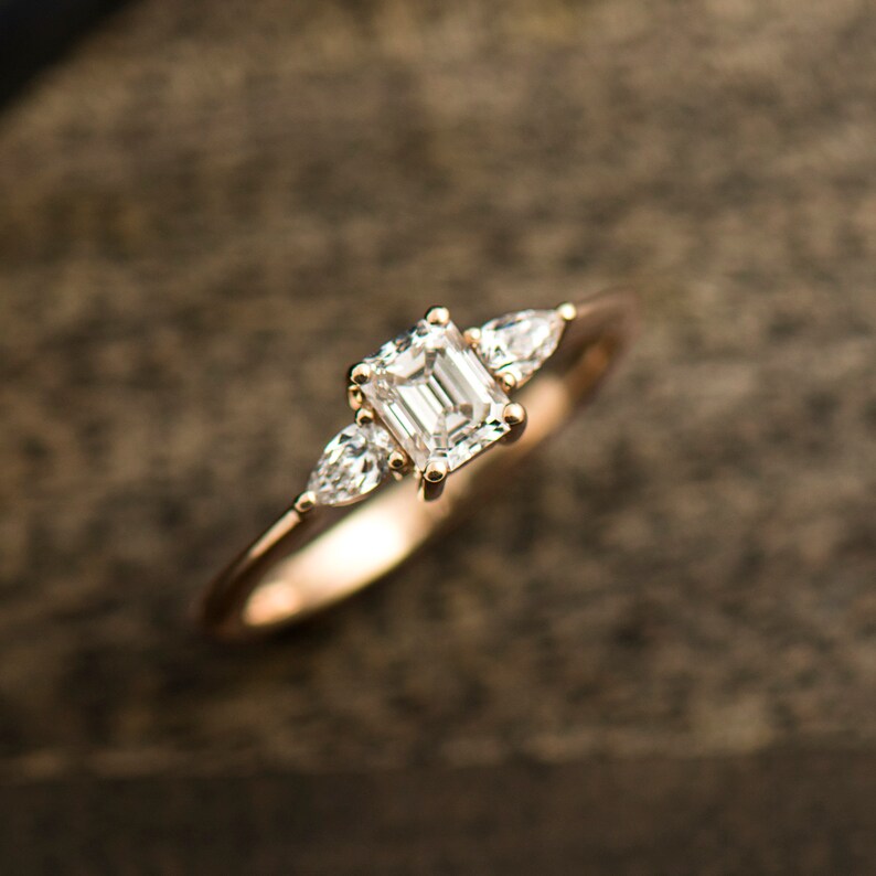May include: A gold engagement ring with an emerald cut diamond and two pear-shaped accent diamonds.