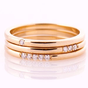 May include: Three gold rings with small diamonds set in the bands. The rings are stacked on top of each other.