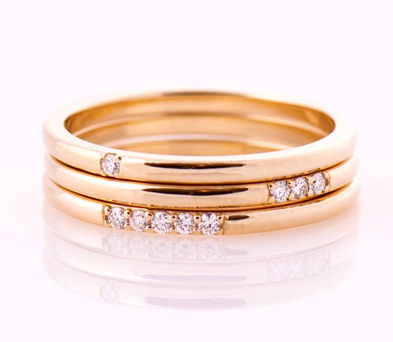 May include: Three gold rings with small diamonds set in the bands. The rings are stacked on top of each other.