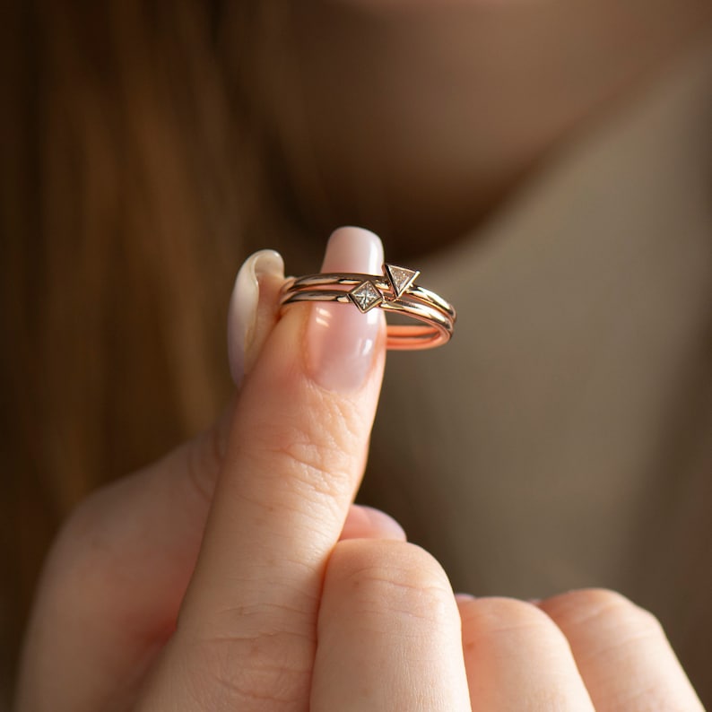 May include: Two gold rings with small triangular diamonds. The rings are stacked on top of each other.