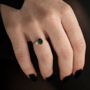 May include: A gold ring with a dark green oval gemstone and two smaller white gemstones on either side.