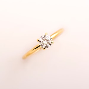 May include: A gold band ring with a single round diamond.