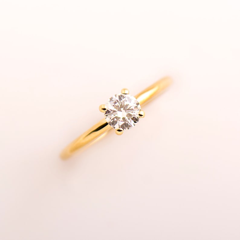 May include: A gold band ring with a single round diamond.