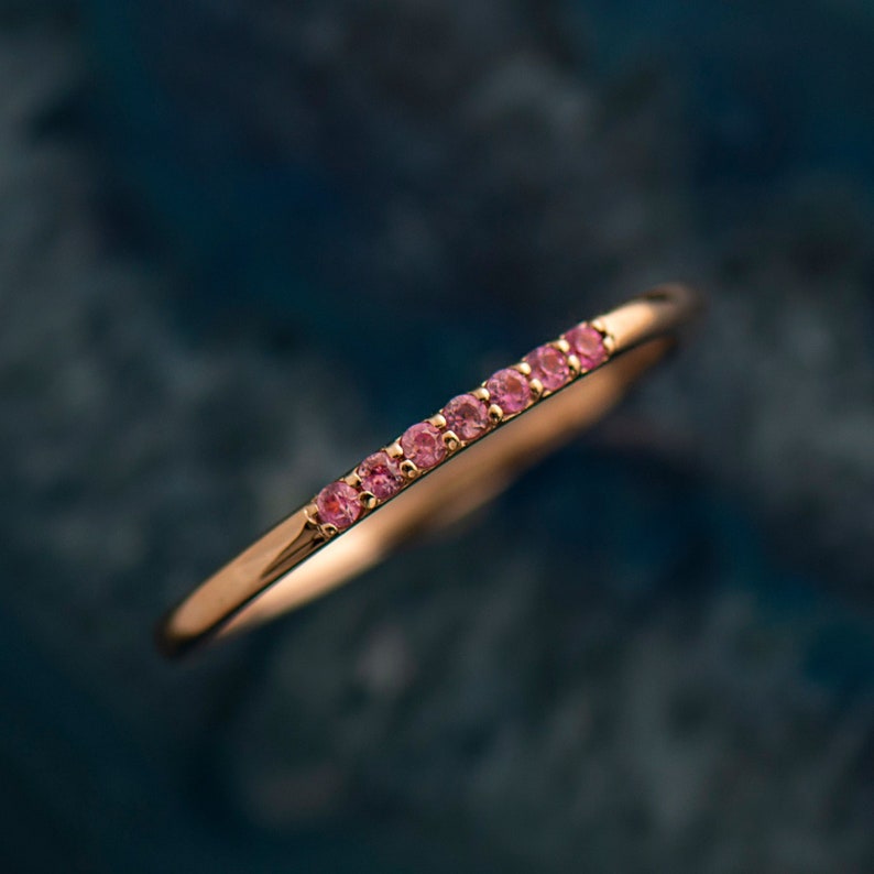 May include: A delicate gold band ring with a row of small pink gemstones.