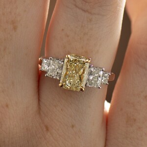 May include: A gold ring with a large, rectangular, yellow diamond in the center and two smaller, square, white diamonds on either side.