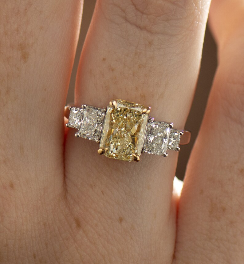 May include: A gold ring with a large, rectangular, yellow diamond in the center and two smaller, square, white diamonds on either side.