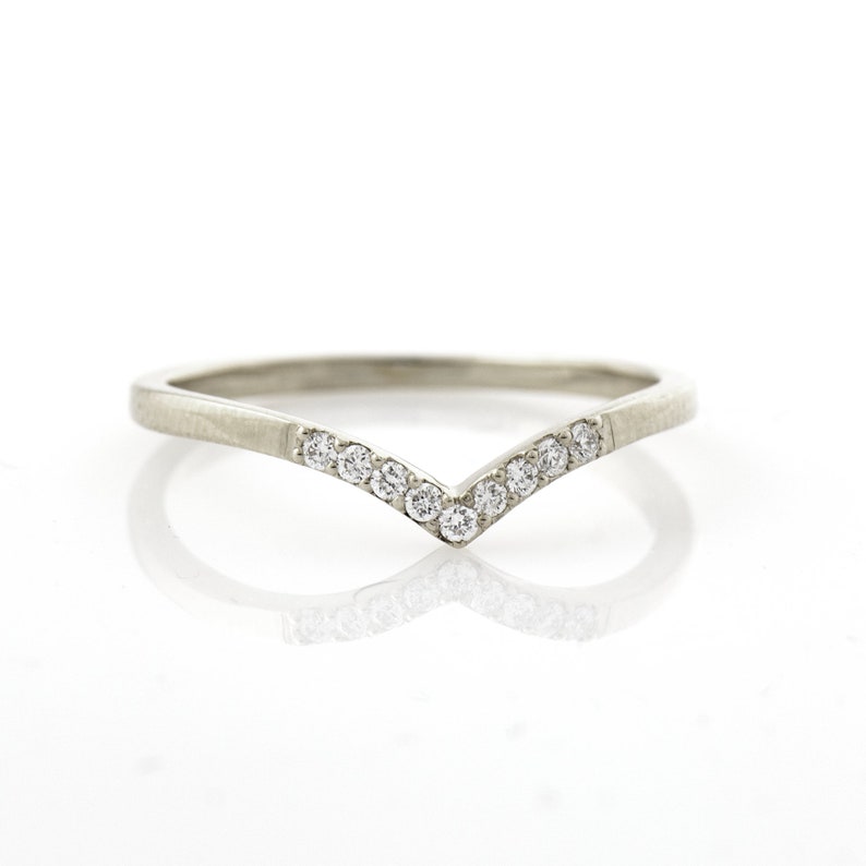 May include: A silver band ring with a V-shaped row of small diamonds.