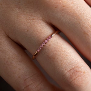 May include: A delicate rose gold ring with a row of small pink gemstones.