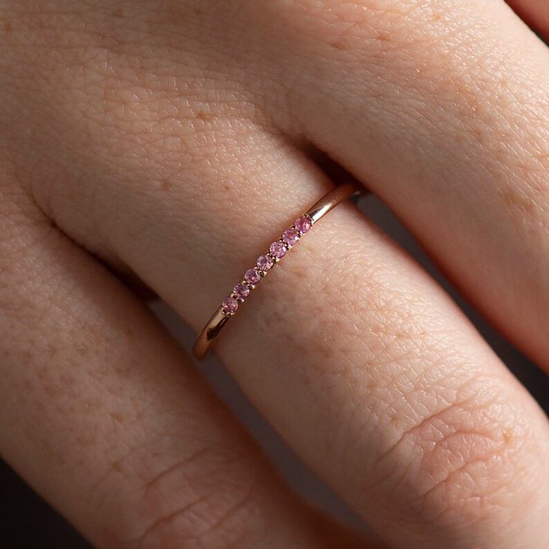 May include: A delicate rose gold ring with a row of small pink gemstones.