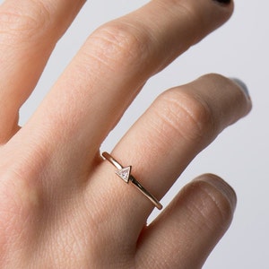 May include: A delicate gold ring with a small triangular diamond set in the center.