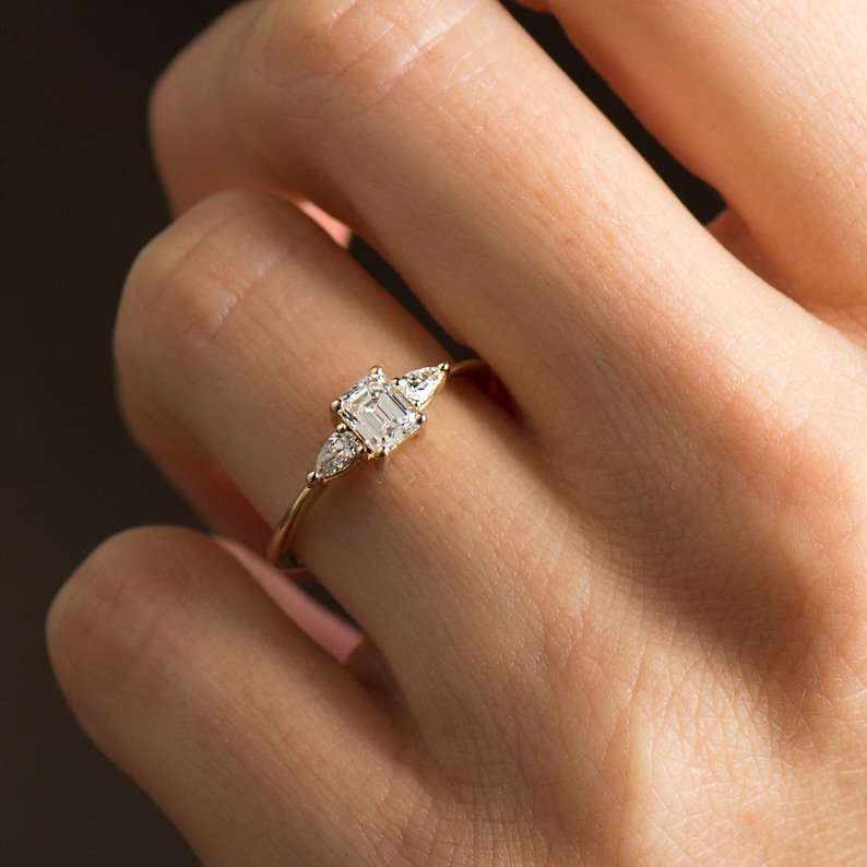 May include: A gold ring with a large emerald-cut diamond and two smaller pear-shaped diamonds on either side.