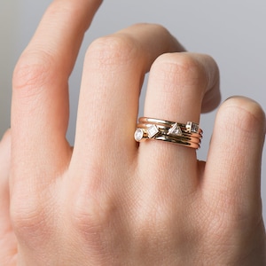 May include: A set of four gold stacking rings with small diamonds. The rings are worn on the ring finger of a hand.