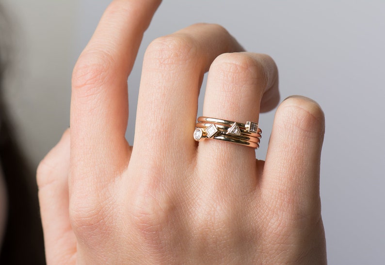 May include: A set of four gold stacking rings with small diamonds. The rings are worn on the ring finger of a hand.