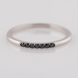 Peut inclure: Une fine bande argent&eacute;e avec une rang&eacute;e de diamants noirs sertis en ligne courbe.