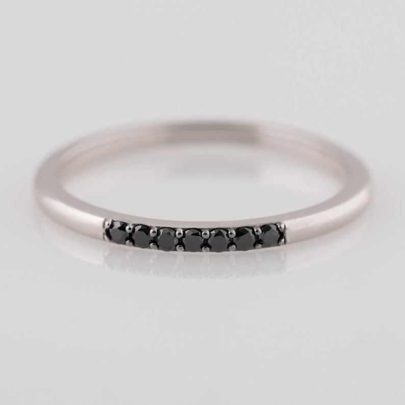 Peut inclure: Une fine bande argent&eacute;e avec une rang&eacute;e de diamants noirs sertis en ligne courbe.