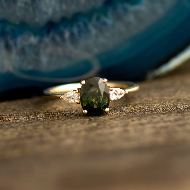 May include: A gold ring with a green oval gemstone and two smaller pear-shaped diamonds on either side.