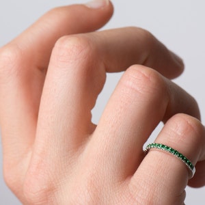 May include: A thin silver band ring with a row of small green gemstones.