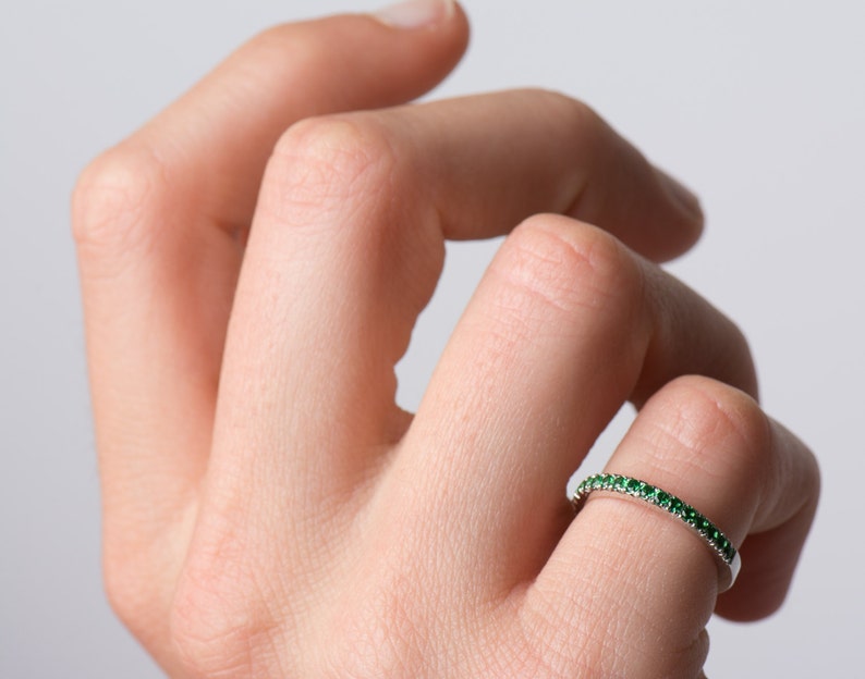 May include: A thin silver band ring with a row of small green gemstones.