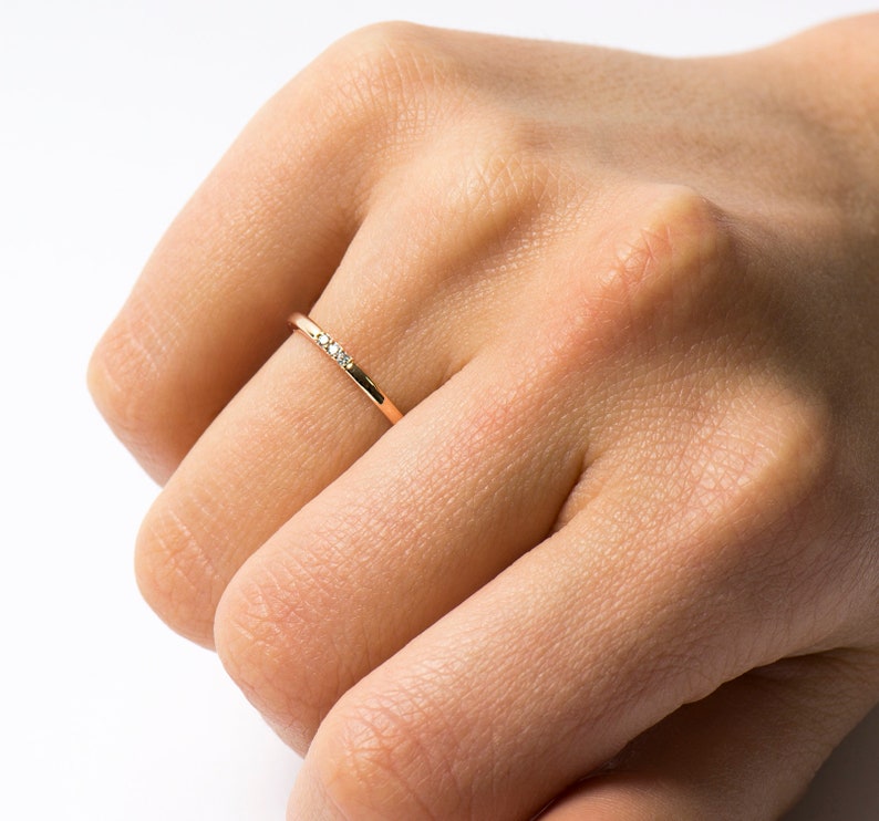 May include: A thin gold band ring with three small diamonds set in a row.