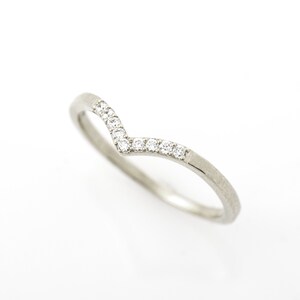 May include: A delicate silver band ring with a V-shaped row of small, clear diamonds.