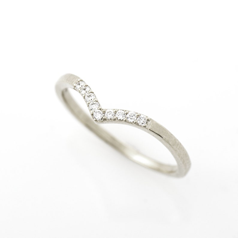 May include: A delicate silver band ring with a V-shaped row of small, clear diamonds.
