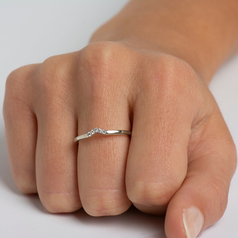 May include: A delicate silver band ring with a row of small diamonds set in a curved shape.