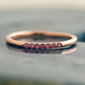 May include: A delicate rose gold band with a row of small pink gemstones.
