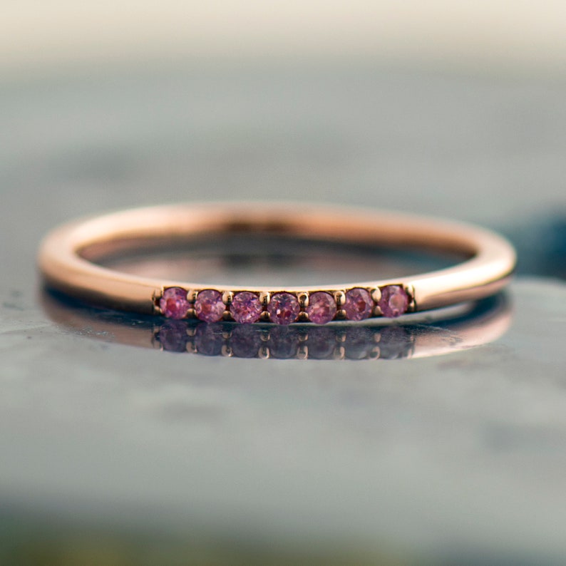 May include: A delicate rose gold band with a row of small pink gemstones.