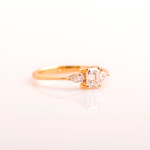 May include: A gold ring with a large emerald-cut diamond and two smaller pear-shaped diamonds on either side.