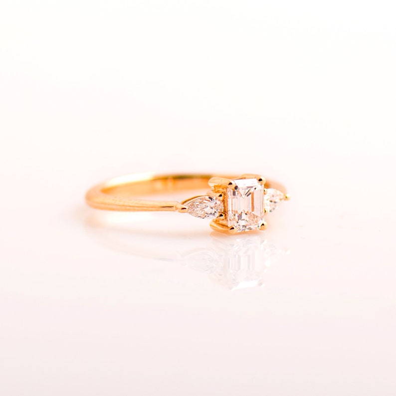 May include: A gold ring with a large emerald-cut diamond and two smaller pear-shaped diamonds on either side.
