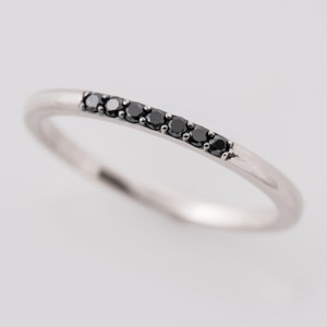 Peut inclure: Une fine bague en argent avec une rang&eacute;e de petits diamants noirs.