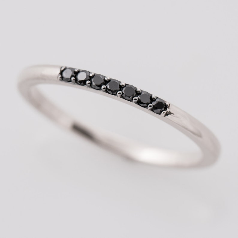 Peut inclure: Une fine bague en argent avec une rang&eacute;e de petits diamants noirs.