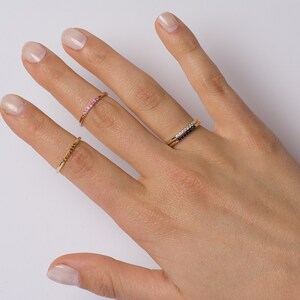 Peut inclure: Une main portant trois bagues en or. La bague sur l'index est sertie de pierres roses, la bague sur le majeur est sertie de pierres noires et la bague sur l'annulaire est une simple bande.