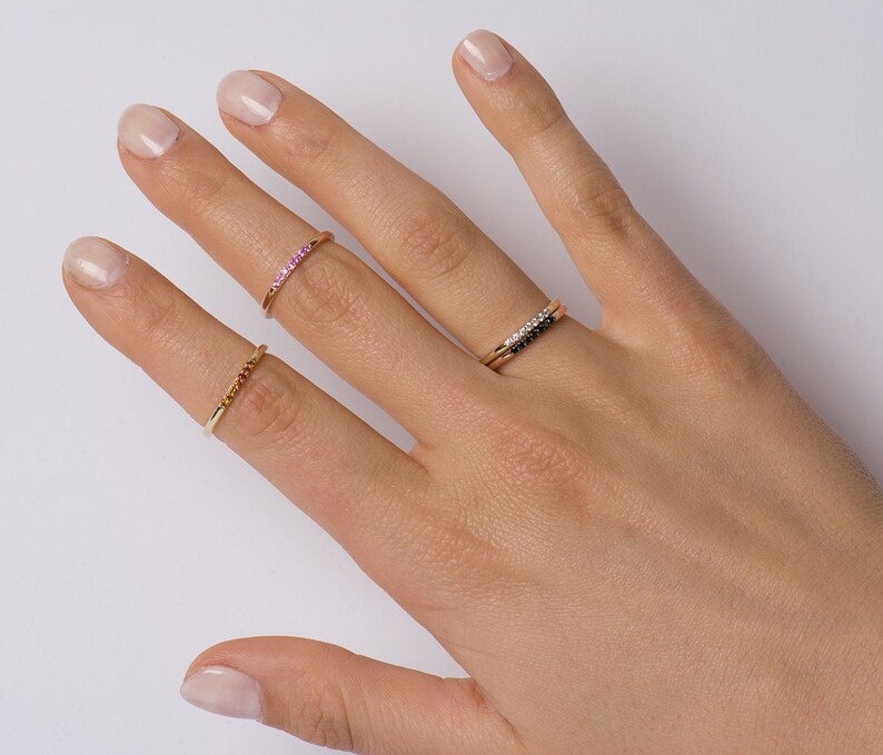 Peut inclure: Une main portant trois bagues en or. La bague sur l'index est sertie de pierres roses, la bague sur le majeur est sertie de pierres noires et la bague sur l'annulaire est une simple bande.