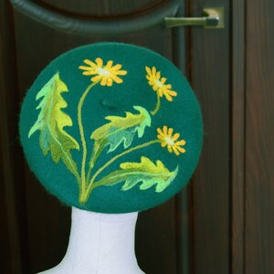 May include: A green felt beret with yellow and green embroidered flowers.