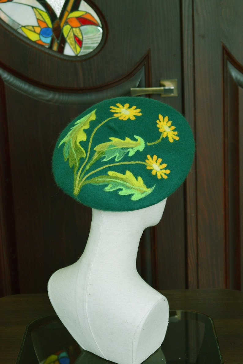 May include: A green felt beret with yellow embroidered flowers. The beret is on a white mannequin head.