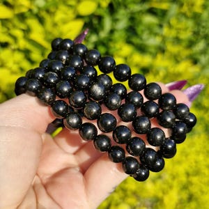 Puede incluir: Un brazalete de piedras preciosas negras con múltiples hileras de cuentas redondas. Las cuentas tienen un brillo sutil y están dispuestas en un patrón en capas.