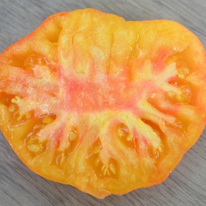 May include: A cross-section of a yellow tomato with a red center and visible seeds.