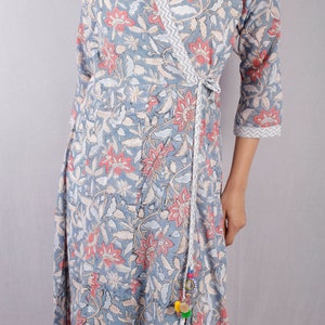 May include: A gray wrap dress with a floral print and a white tie. The dress has a V-neckline and three-quarter sleeves. The tie has a tassel with colorful pom-poms.