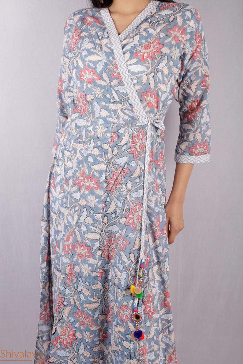 May include: A gray wrap dress with a floral print and a white tie. The dress has a V-neckline and three-quarter sleeves. The tie has a tassel with colorful pom-poms.