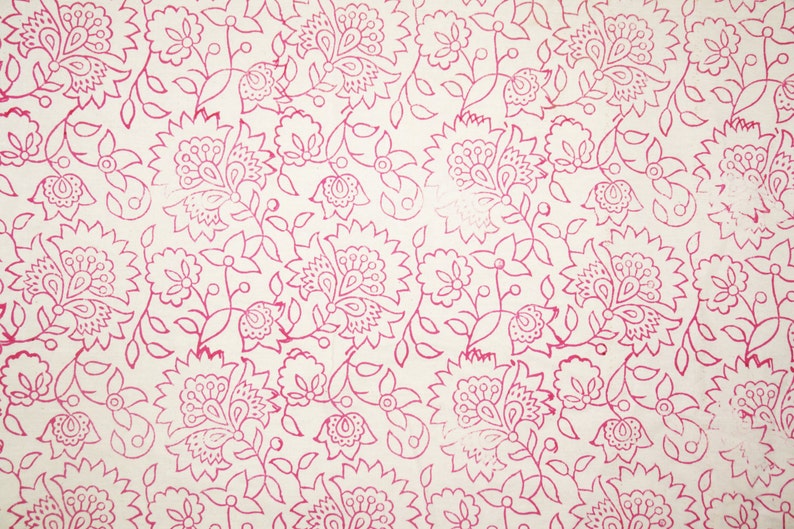 May include: A cream-colored fabric with a repeating pattern of pink floral designs. The pattern includes stylized flowers, leaves, and vines, creating a detailed and intricate visual texture. The floral elements are outlined in a vibrant pink.
