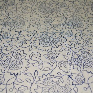 May include: Close-up of a white fabric with a repeating pattern of blue floral designs. The pattern includes stylized flowers, leaves, and vines, creating a detailed and decorative textile.