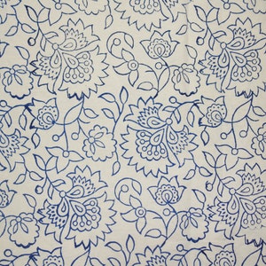 May include: Cream-colored fabric with a repeating pattern of blue floral designs. The pattern includes large, stylized flowers, smaller blossoms, and connecting vines with leaves. The design is evenly spaced across the fabric.