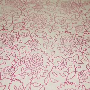 May include: Close-up of a cream-colored fabric with a repeating floral pattern in a vibrant pink hue. The design features stylized flowers, leaves, and vines, creating a delicate and intricate textile design.